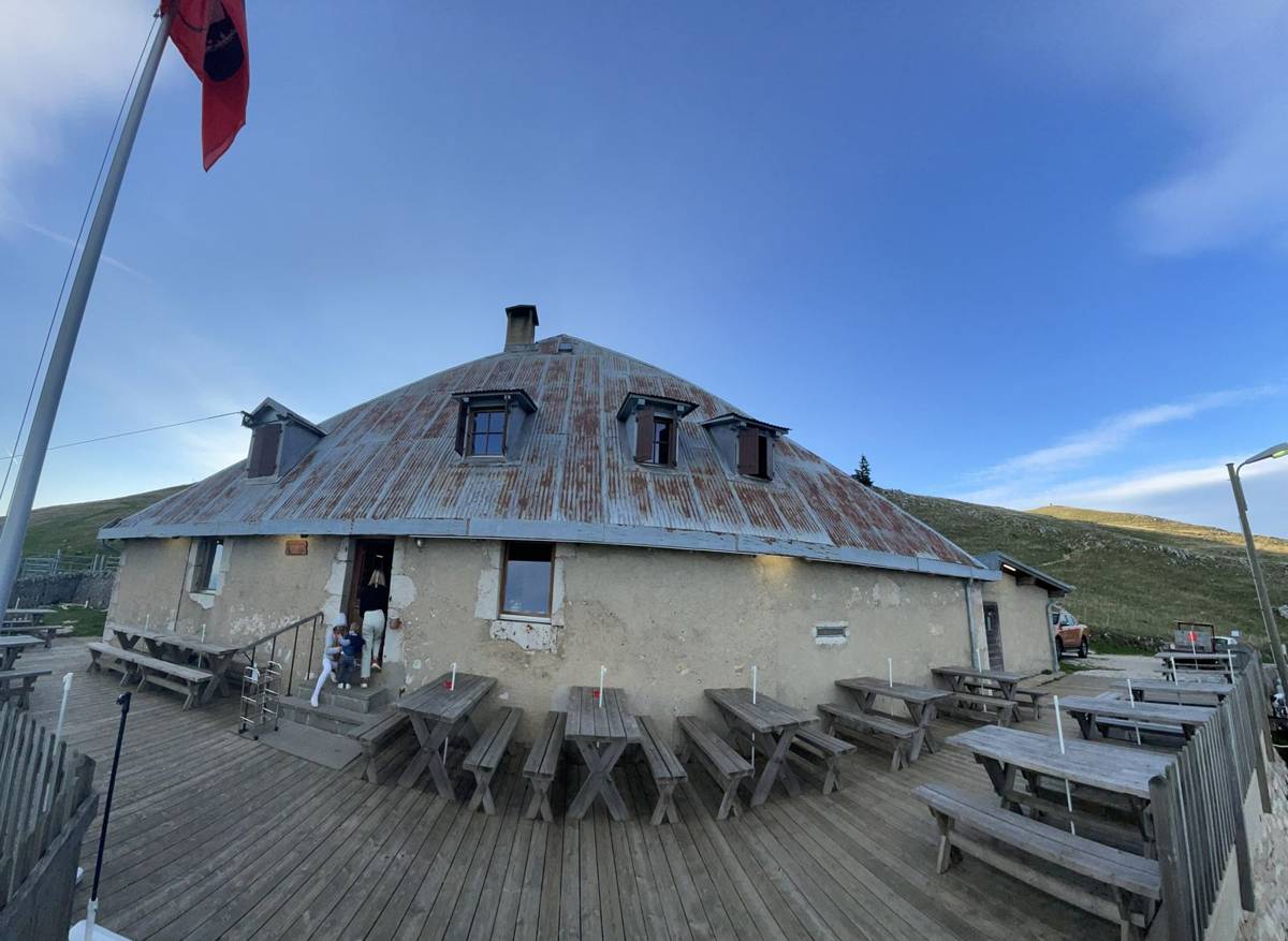 La terrasse en bois devant le chalet, tables et bancs alignés sous le ciel bleu